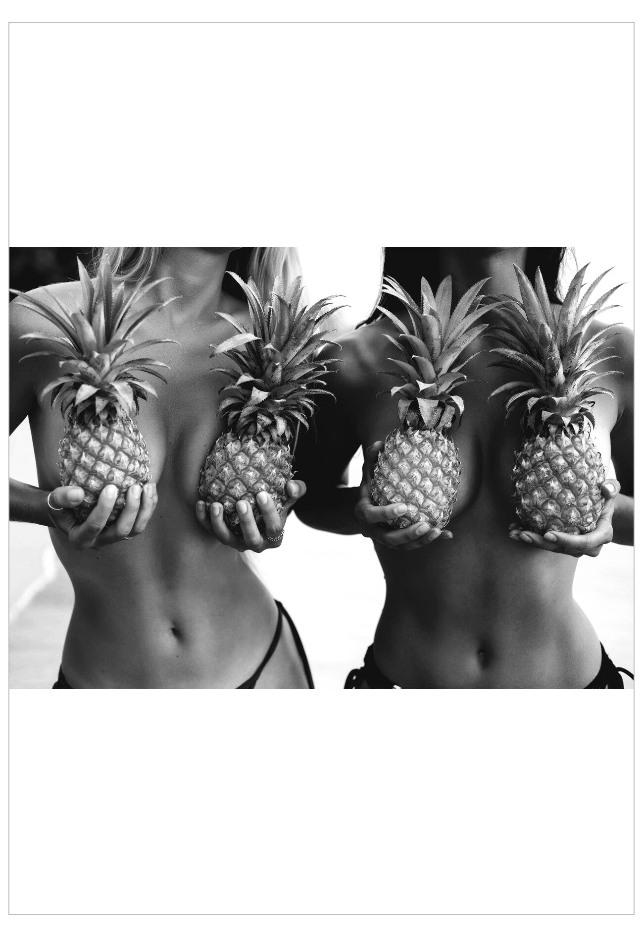 Black and white image of two people holding pineapples in front of their faces.