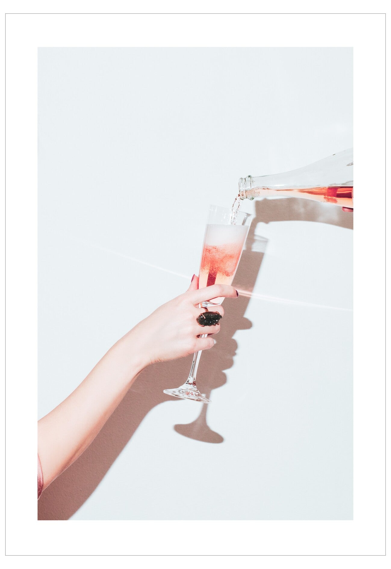 Person pouring pink champagne into a glass against a white background