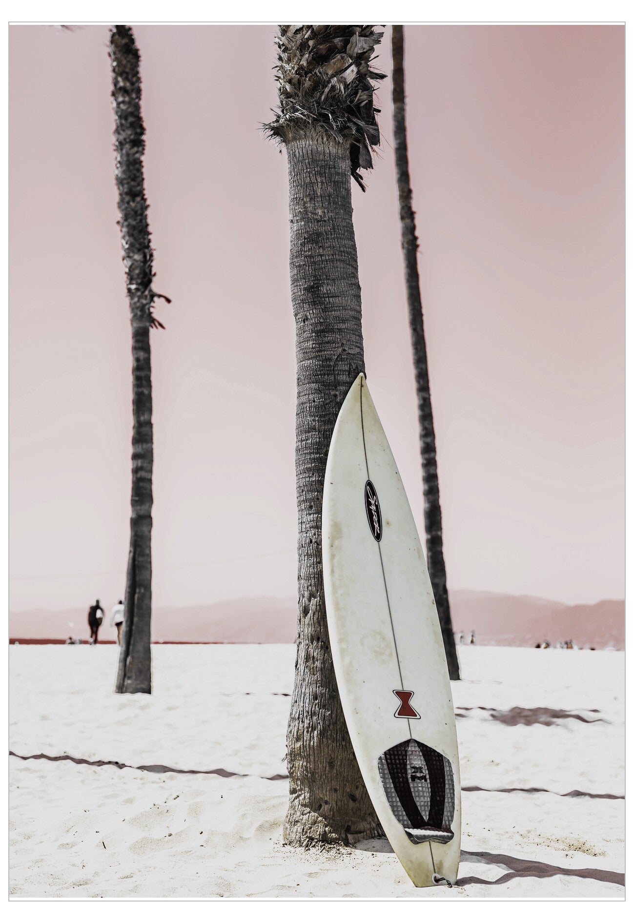 Surfboard leaning against a palm tree on a beach with a pink sky