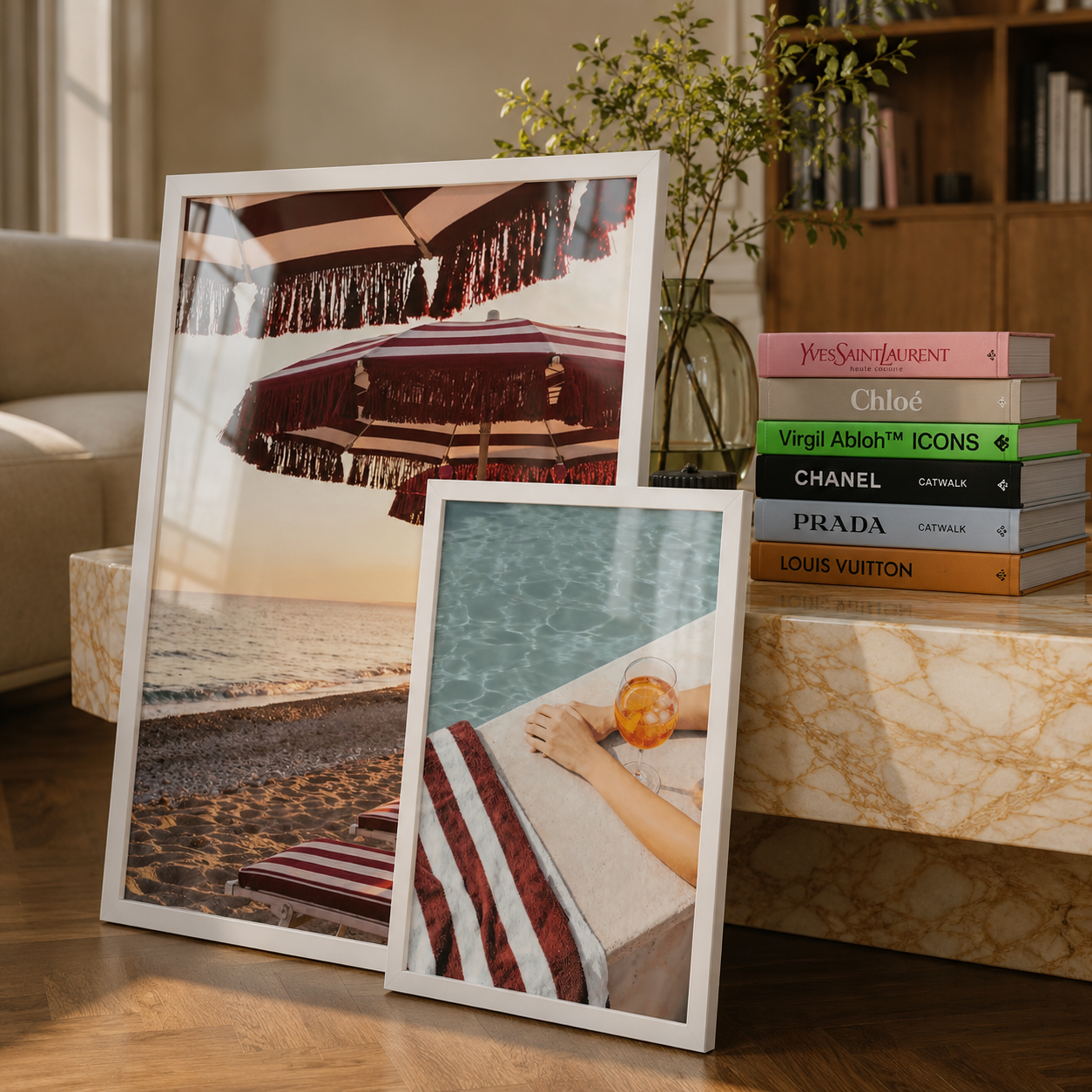 Two framed pictures on a table with books stacked behind them.
