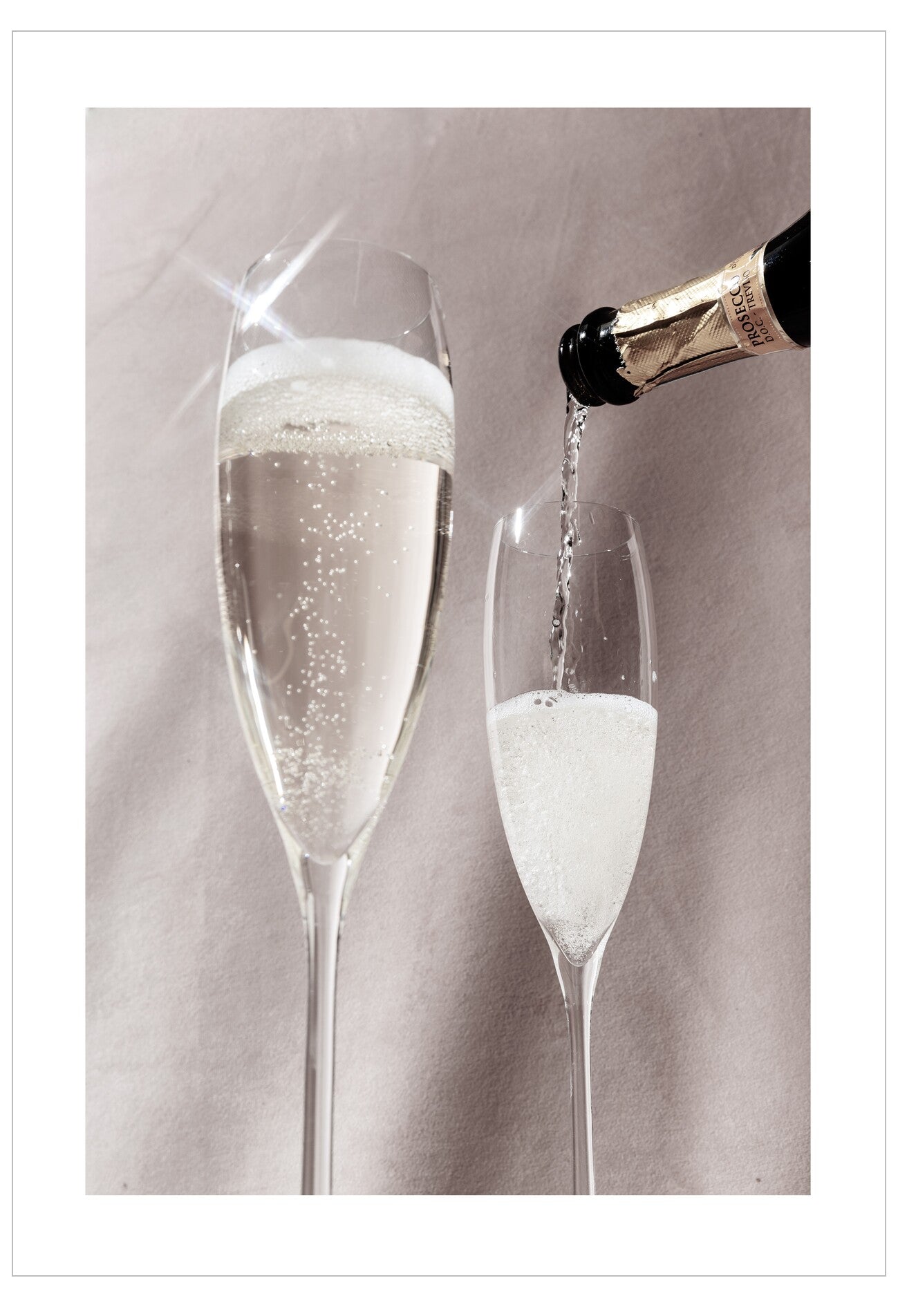 Two champagne flutes being filled with champagne against a neutral background