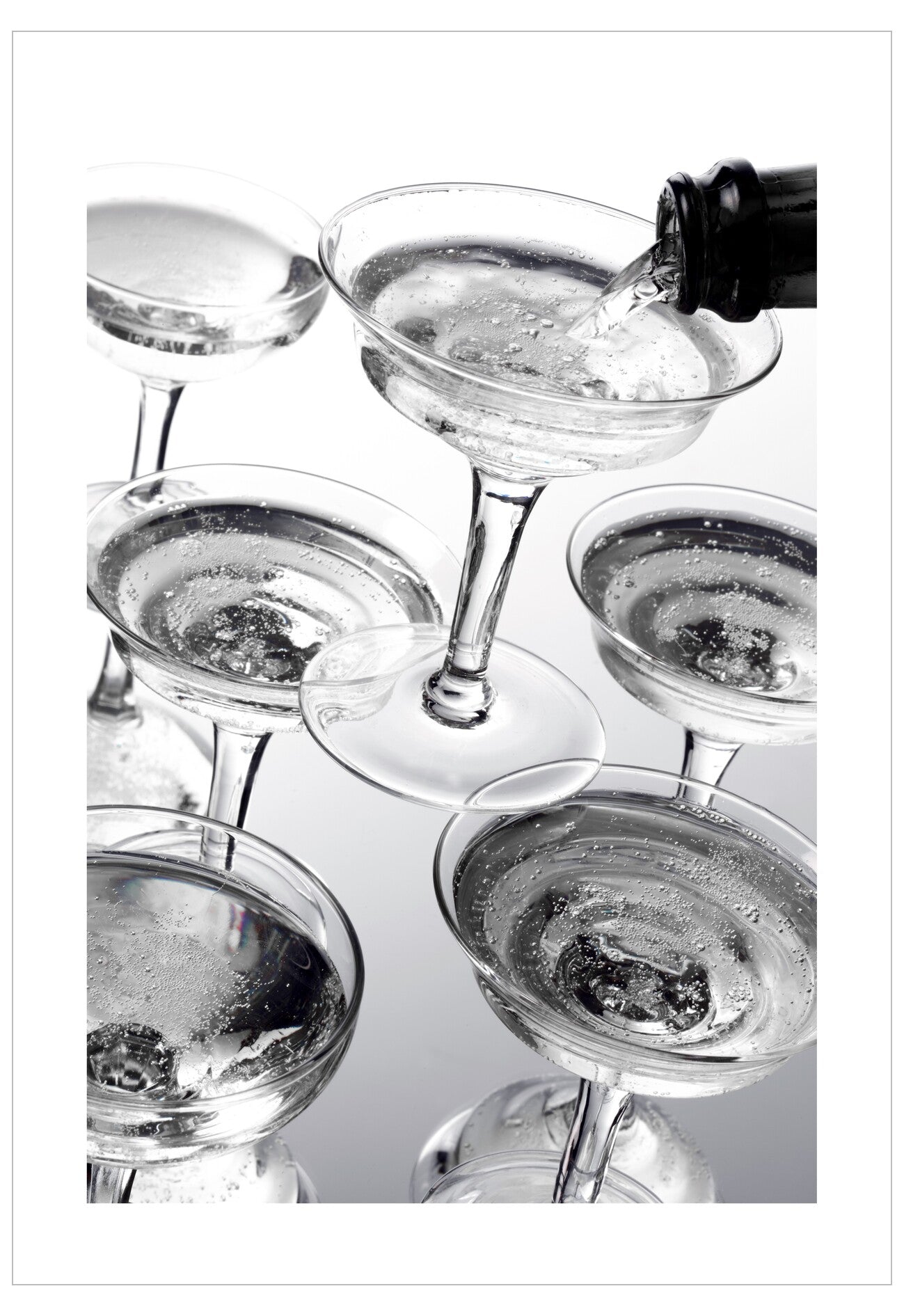 Cocktail being poured into a glass with other glasses around on a reflective surface