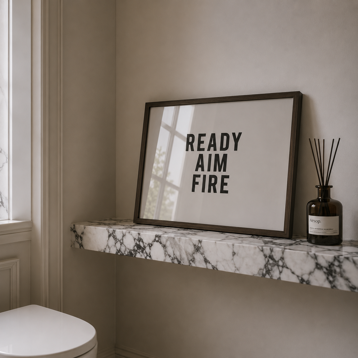 Framed poster with 'READY AIM FIRE' text on a marble shelf in a bathroom.