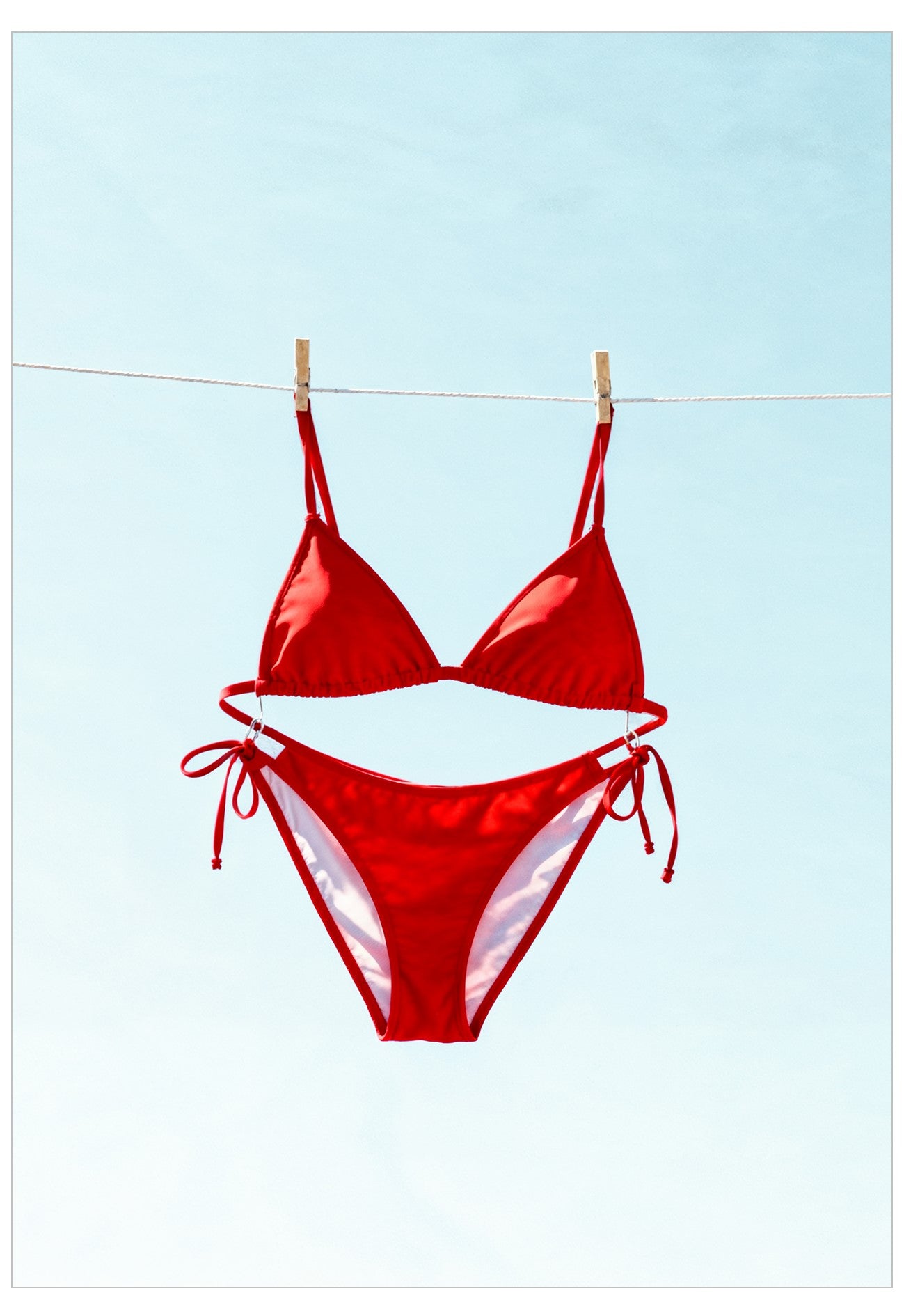 Red bikini hanging on a clothesline against a clear blue sky