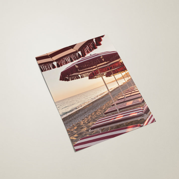Beach towel with striped beach umbrellas and sunset over water design on a light gray background