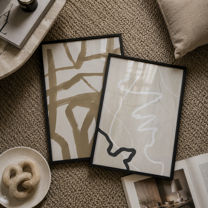 Two framed abstract artworks on a textured surface with a plate and book in the foreground.