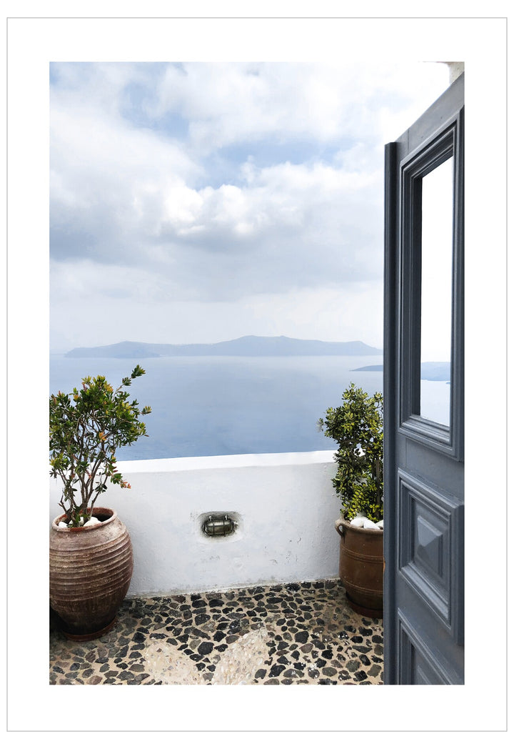 Open door leading to a scenic view of the ocean with white buildings and potted plants.