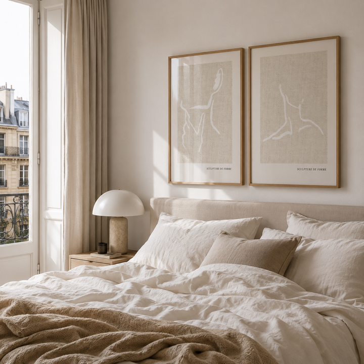 Neatly made bed with beige and white bedding in a bedroom with framed artwork on the wall.