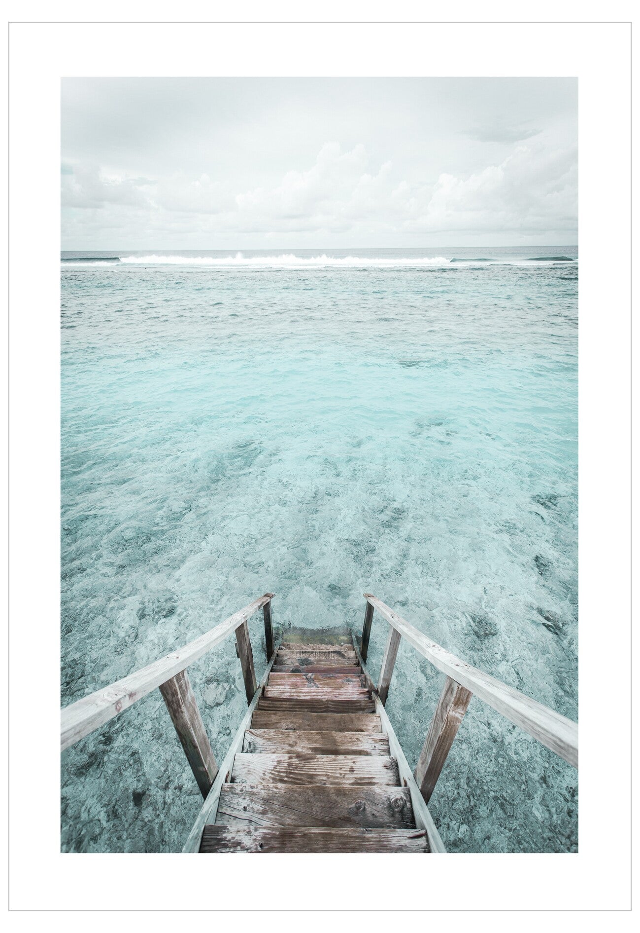 Wooden staircase leading into clear blue water with a white sky.