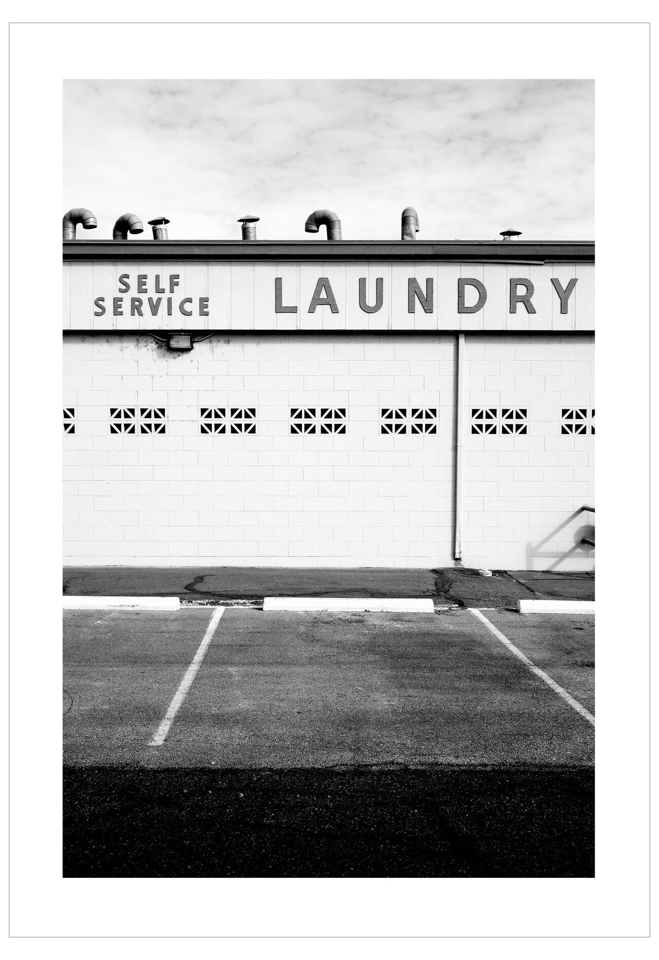 Black and white image of a self-service laundry facility with a sign above the entrance.