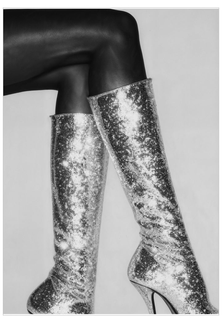 Silver sequin knee-high boots worn with black tights on a light gray background