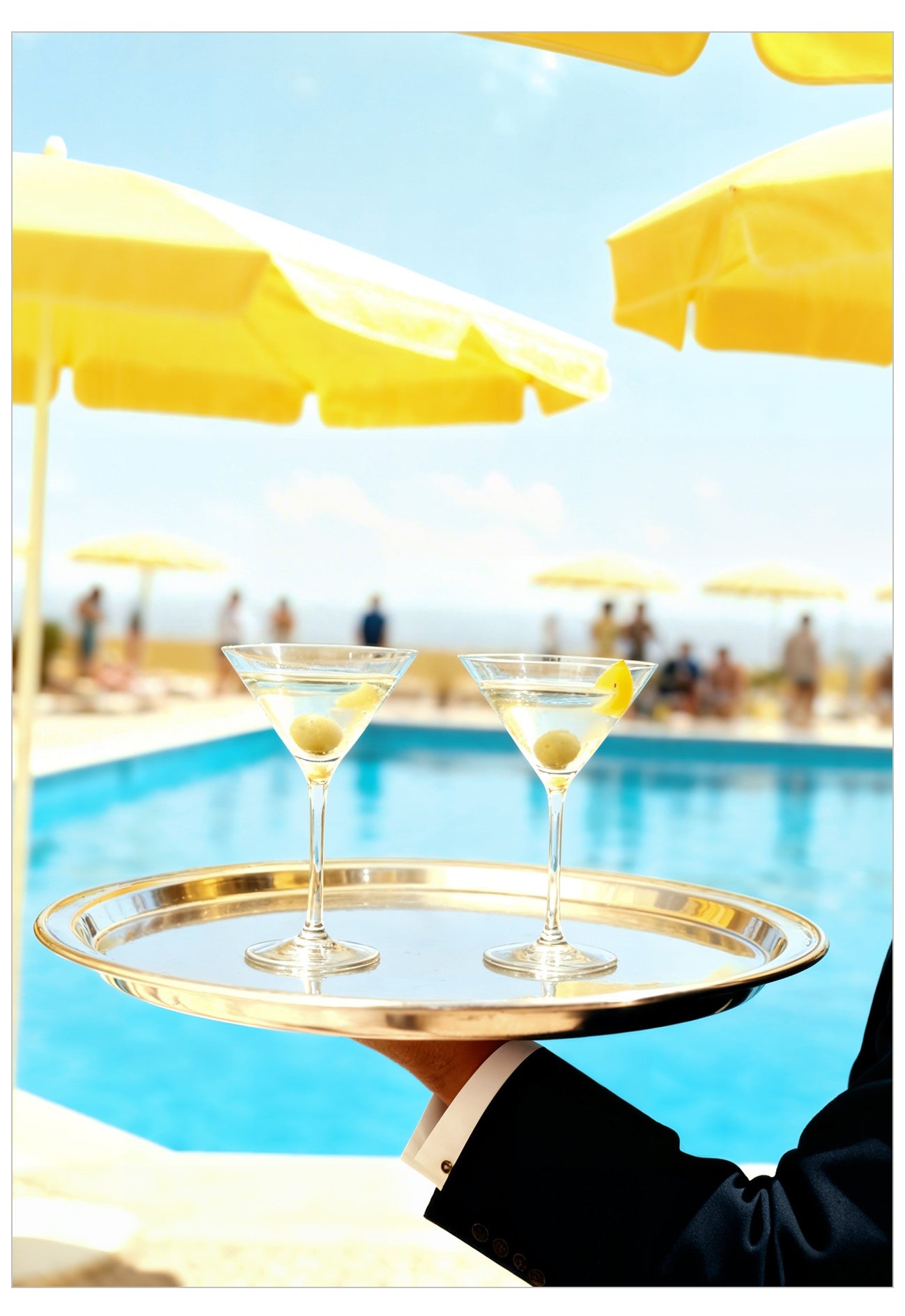 Two martini glasses on a gold tray held by a person by a pool with yellow umbrellas.