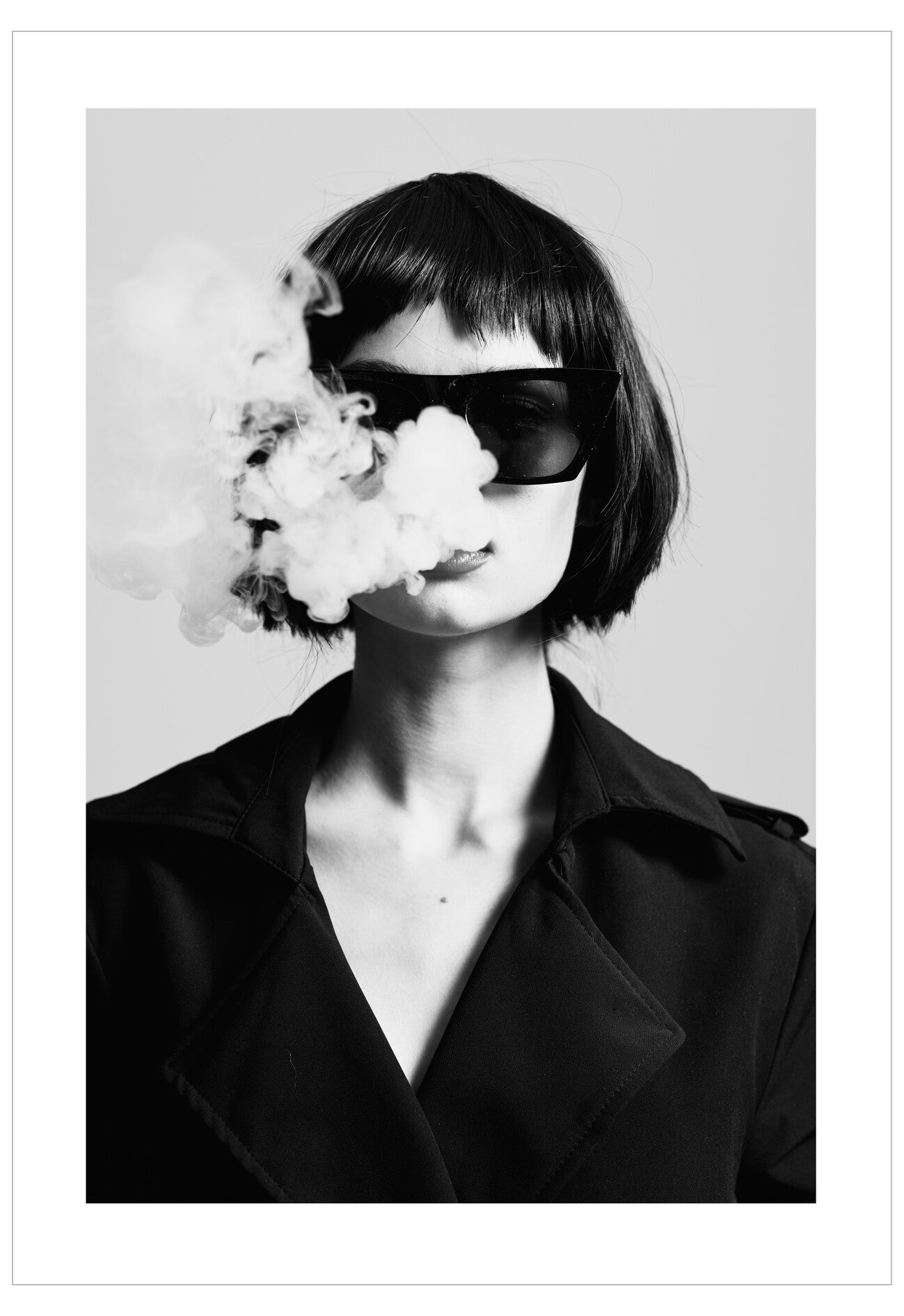 Black and white portrait of a person with smoke coming out of their mouth, wearing sunglasses and a coat.