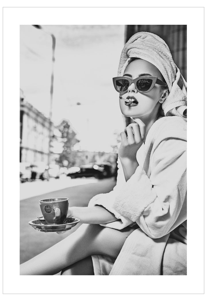 Woman in a robe with a towel on her head, holding a cup, sitting outdoors.