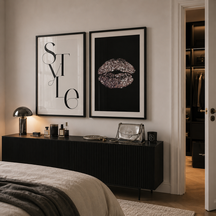 A styled bedroom interior showing two framed wall art prints above a black ribbed console table. The left print has black typography on white, and the right print shows glittery lips on black.