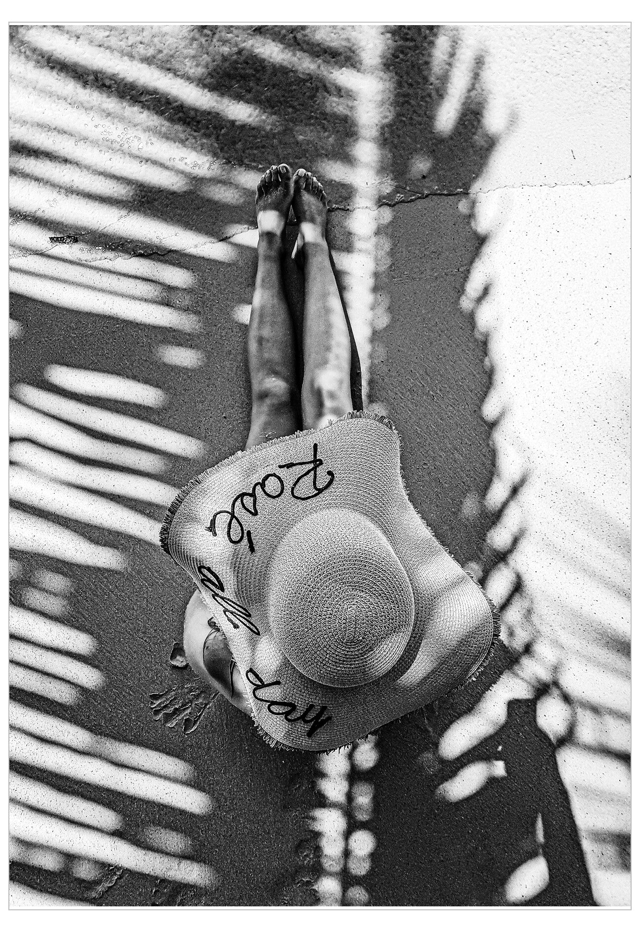 Black and white photo of a person wearing a wide-brimmed hat with text, standing against a palm leaf background.