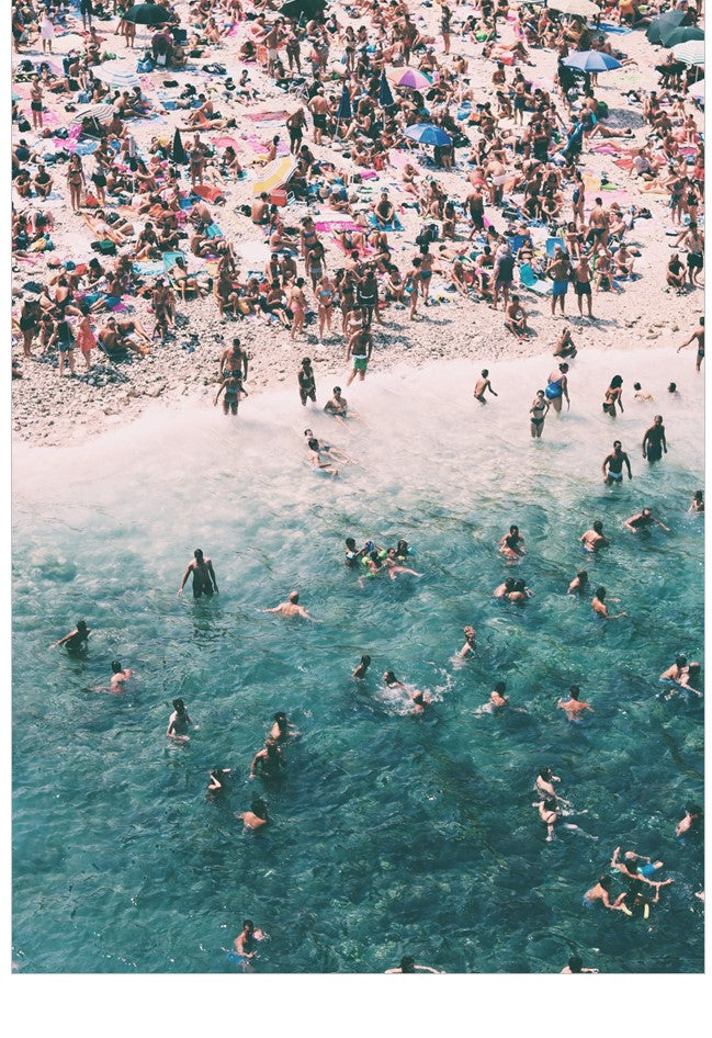 People enjoying a crowded beach with clear blue water.