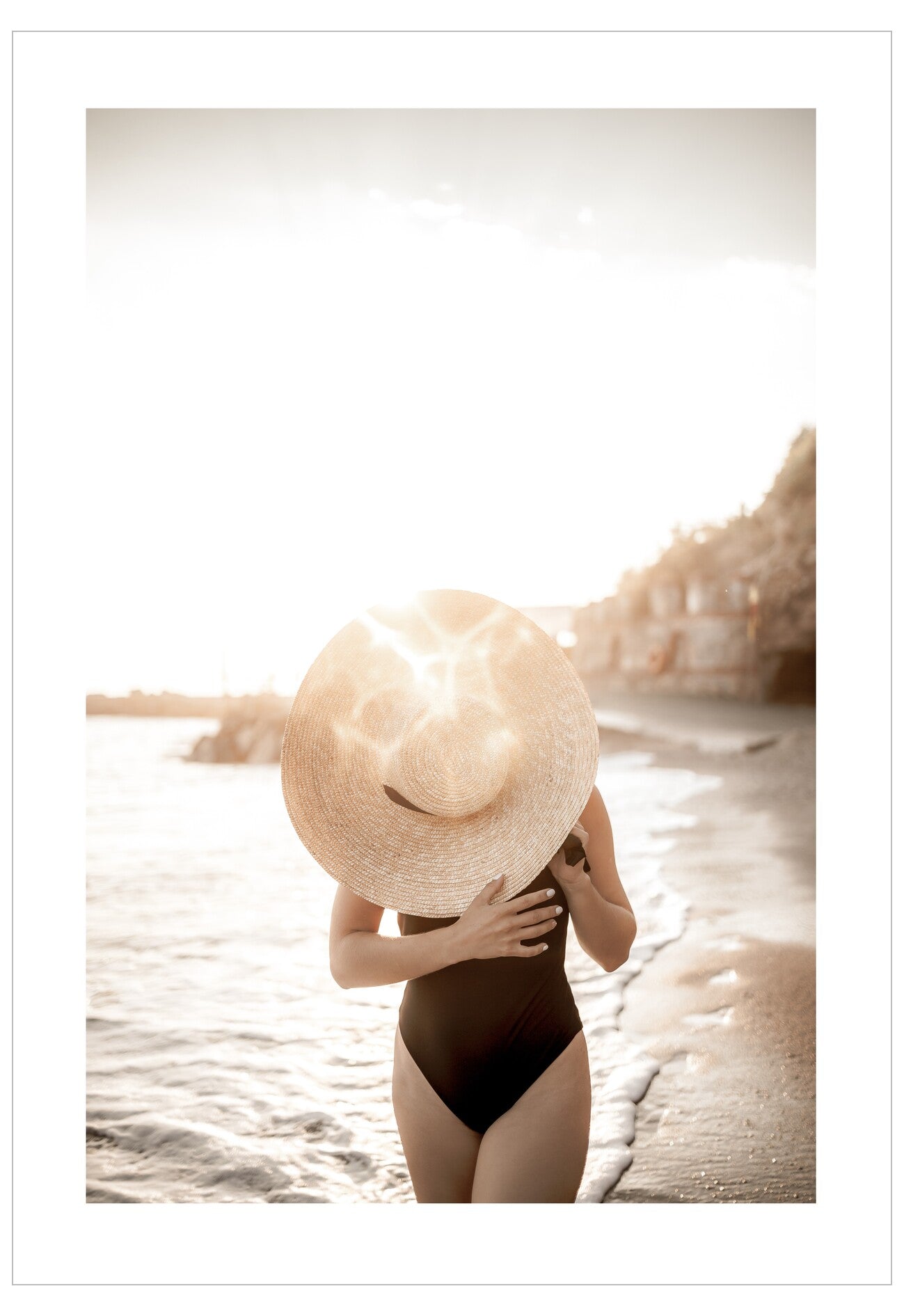 Person wearing a black swimsuit and large sun hat on a beach.