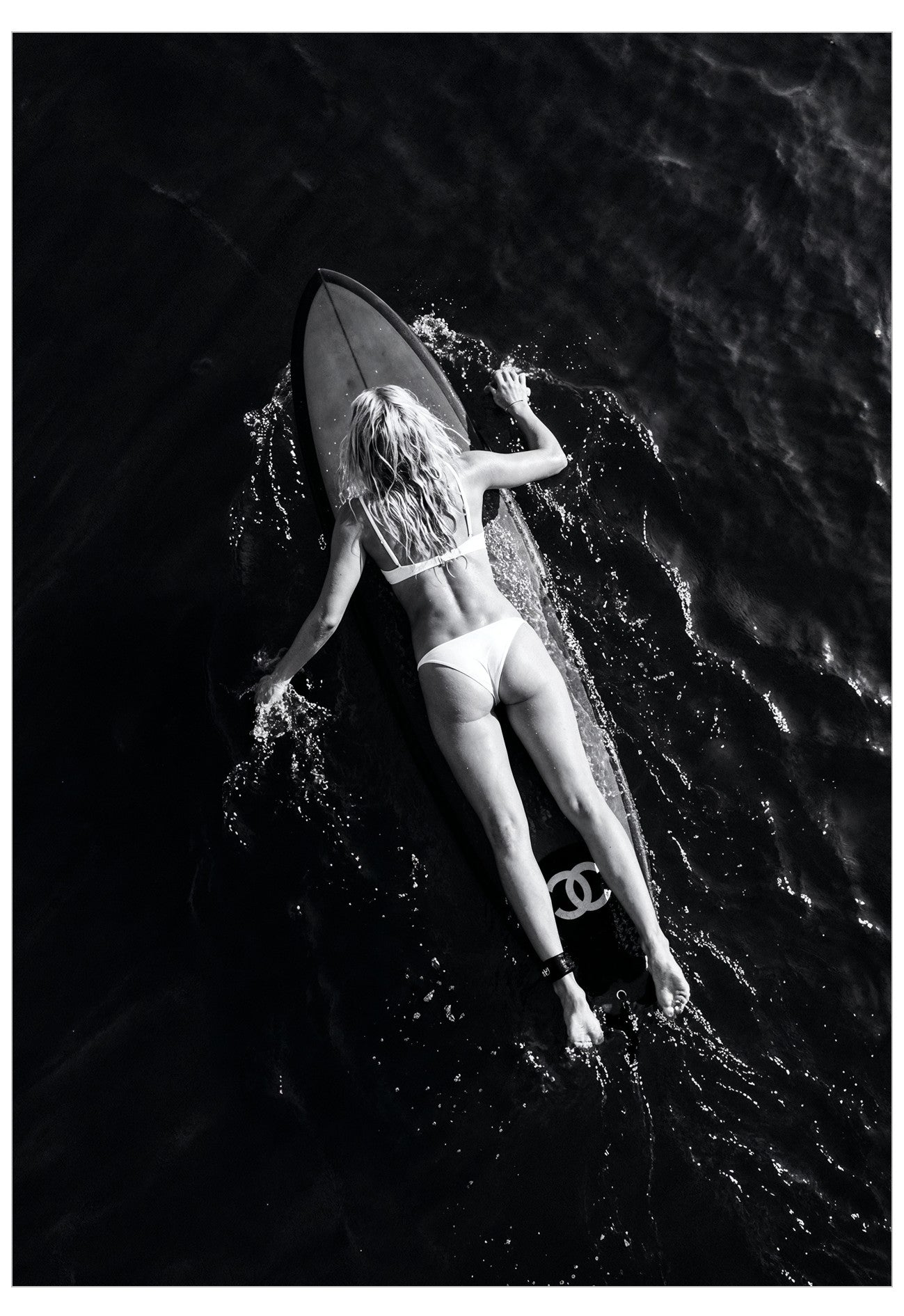 A black and white image of a woman laying on a surfboard in the middle of the ocean