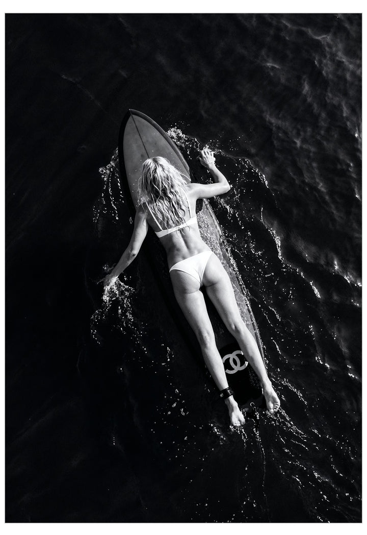 A black and white image of a woman laying on a surfboard in the middle of the ocean