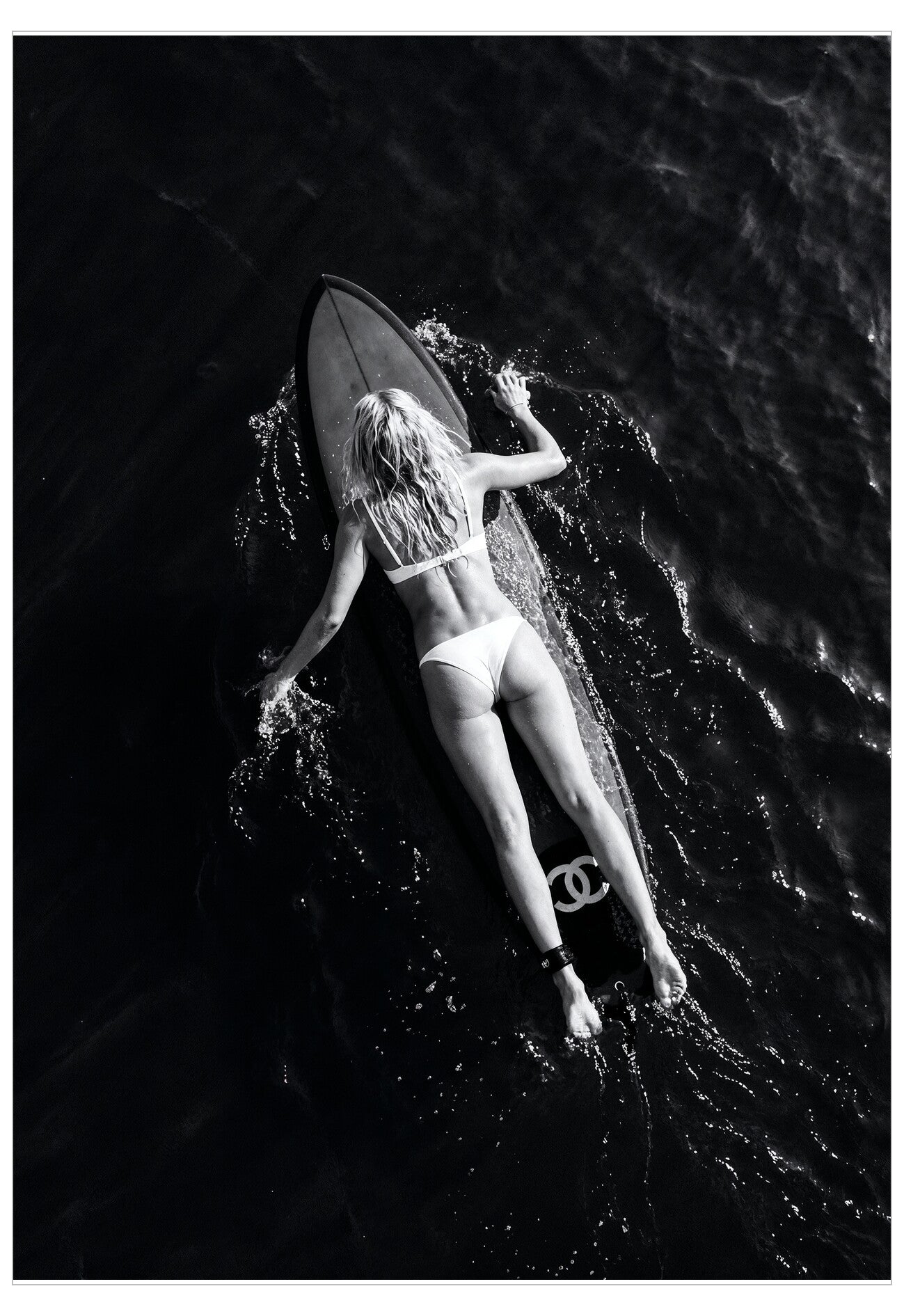 Black and white photo of a person lying on a surfboard in the water