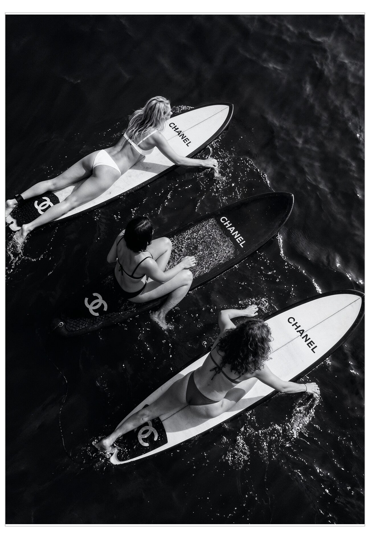 Three women on Chanel branded surfboards in the water.