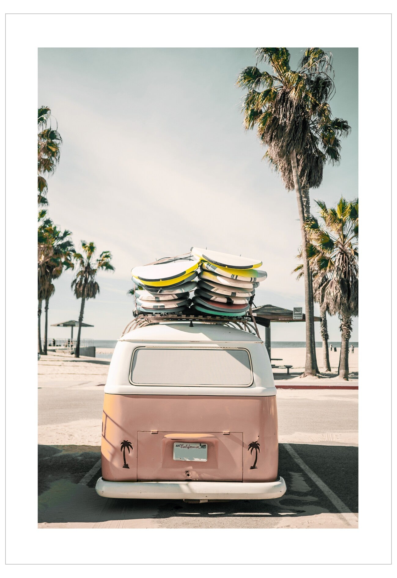 Pink vintage van with surfboards on a beach road lined with palm trees.