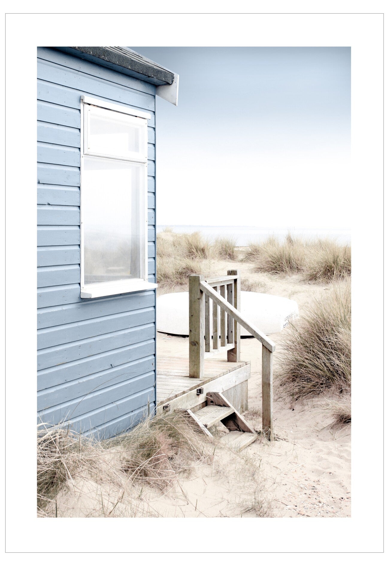 Blue beach hut with wooden steps leading up to it, surrounded by sand and grass.