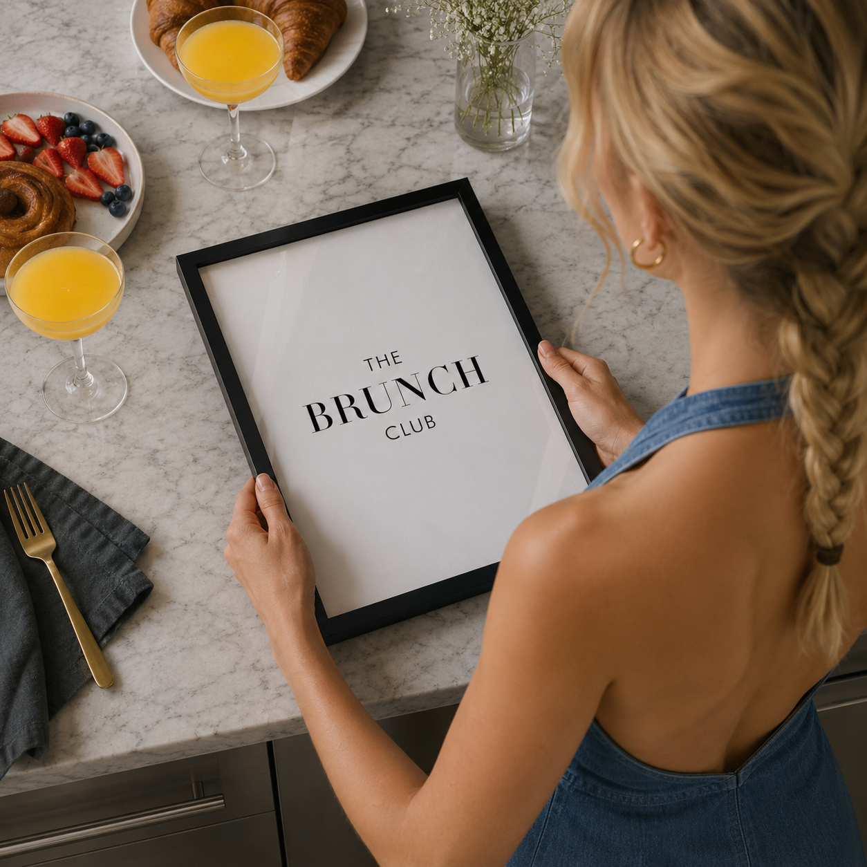 woman holding bruch club poster in a black frame in modern kitchen