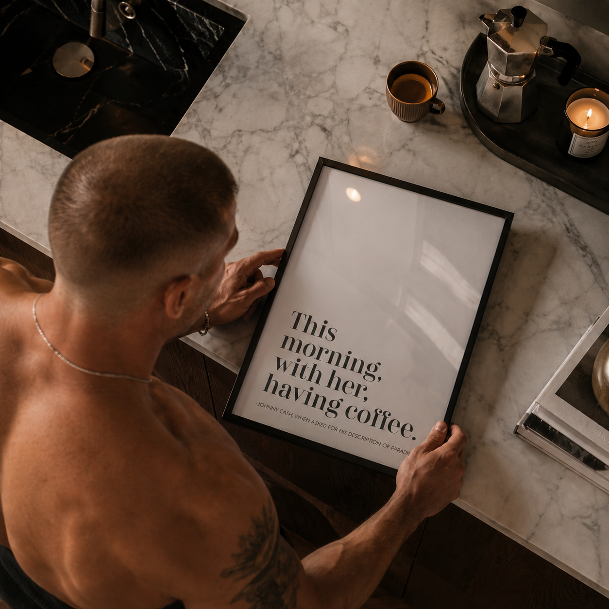 Man holding a framed quote on a marble countertop with coffee and candles.