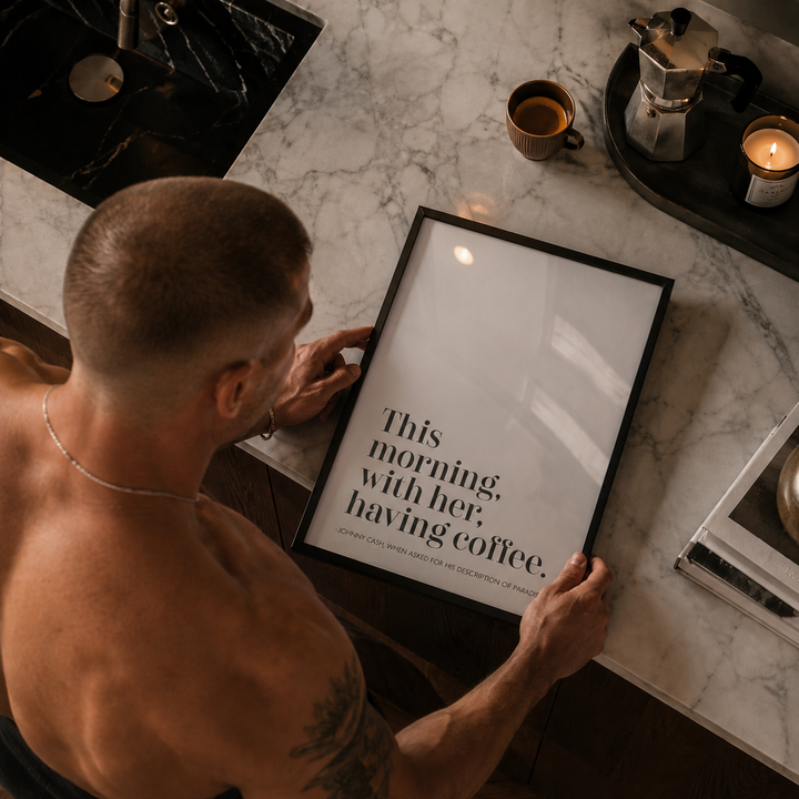 Man holding a framed quote on a marble countertop with coffee and candles.