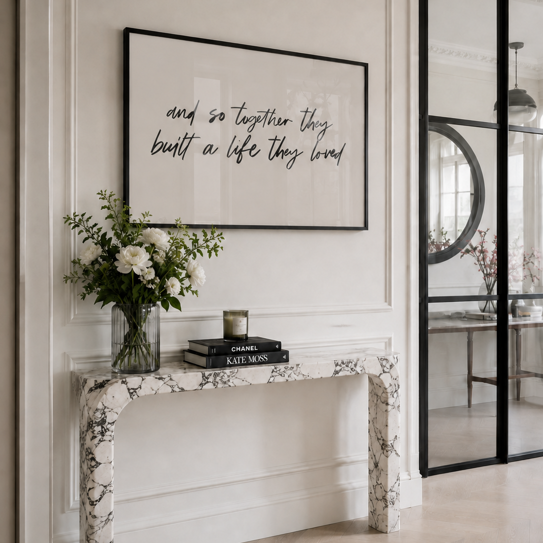 Decorative console table with flowers, books, and a framed quote in a stylish interior setting.
