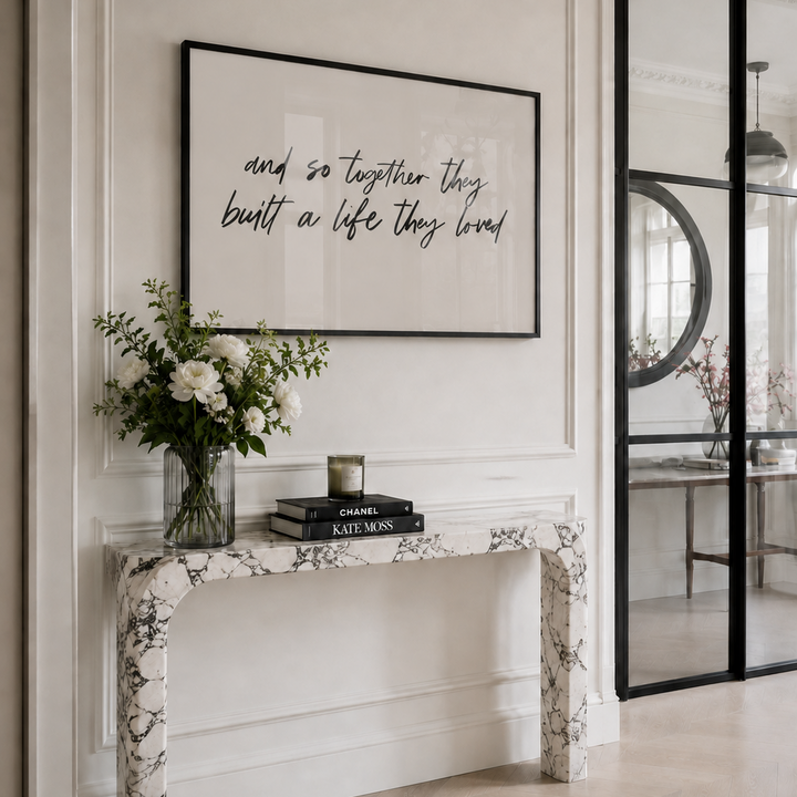 Decorative console table with flowers, books, and a framed quote in a stylish interior setting.