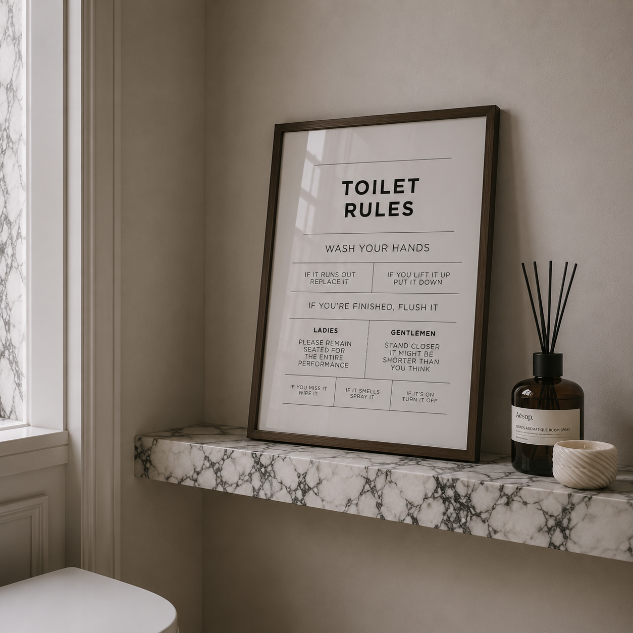 Framed 'Toilet Rules' poster on a marble shelf with decorative items.