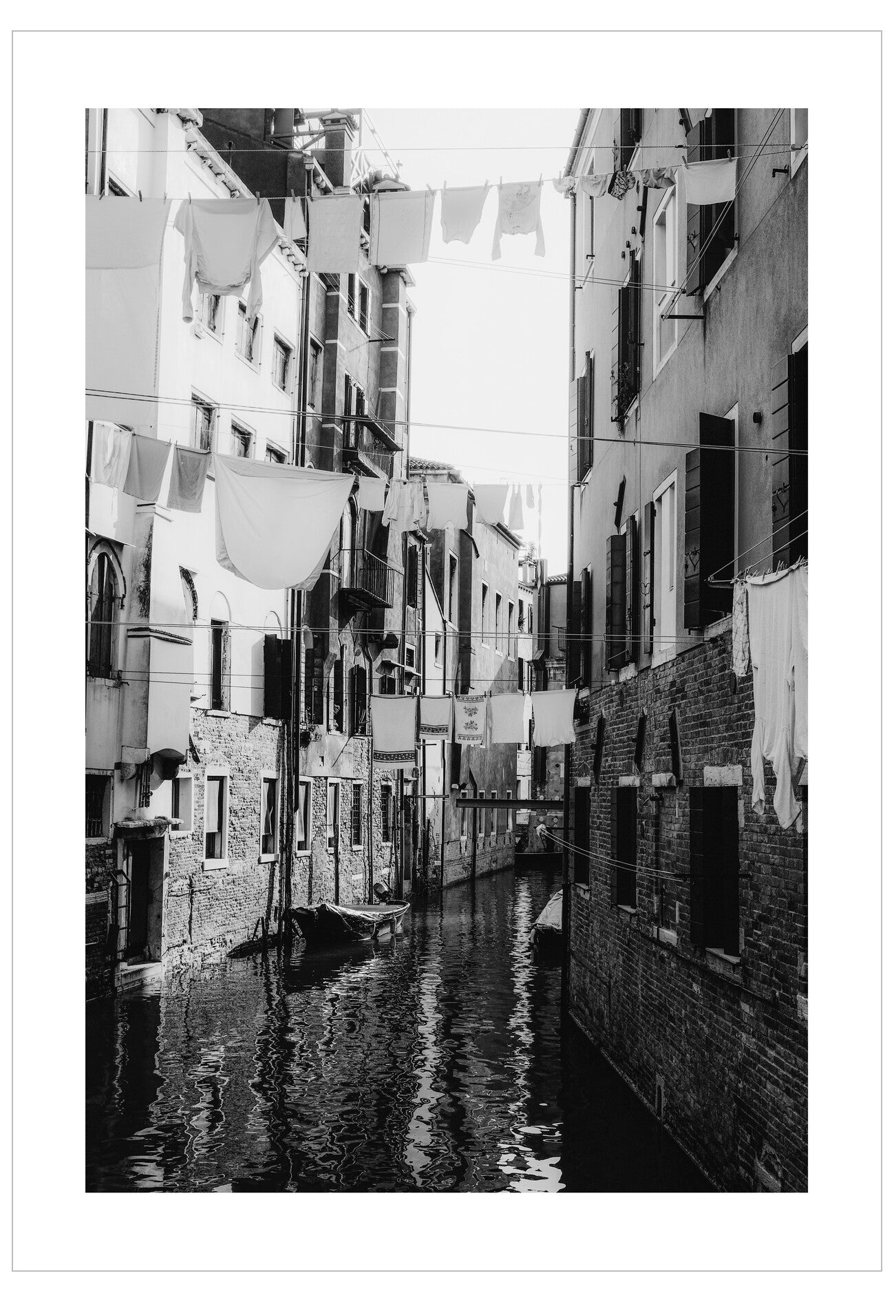 Black and white photo of a narrow canal with buildings on either side and clothes hanging to dry.