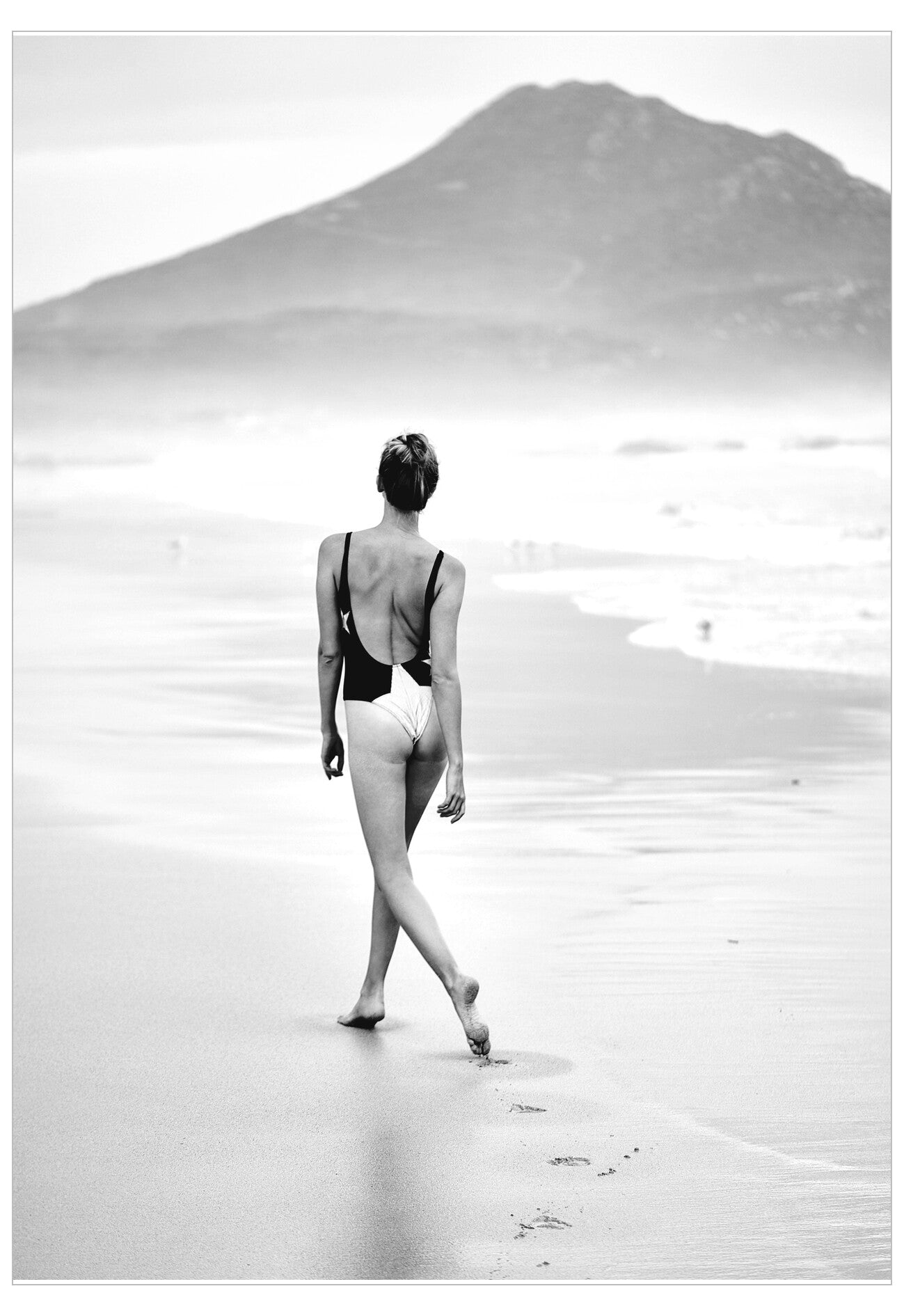 Person in a swimsuit walking on a beach with a mountain in the background