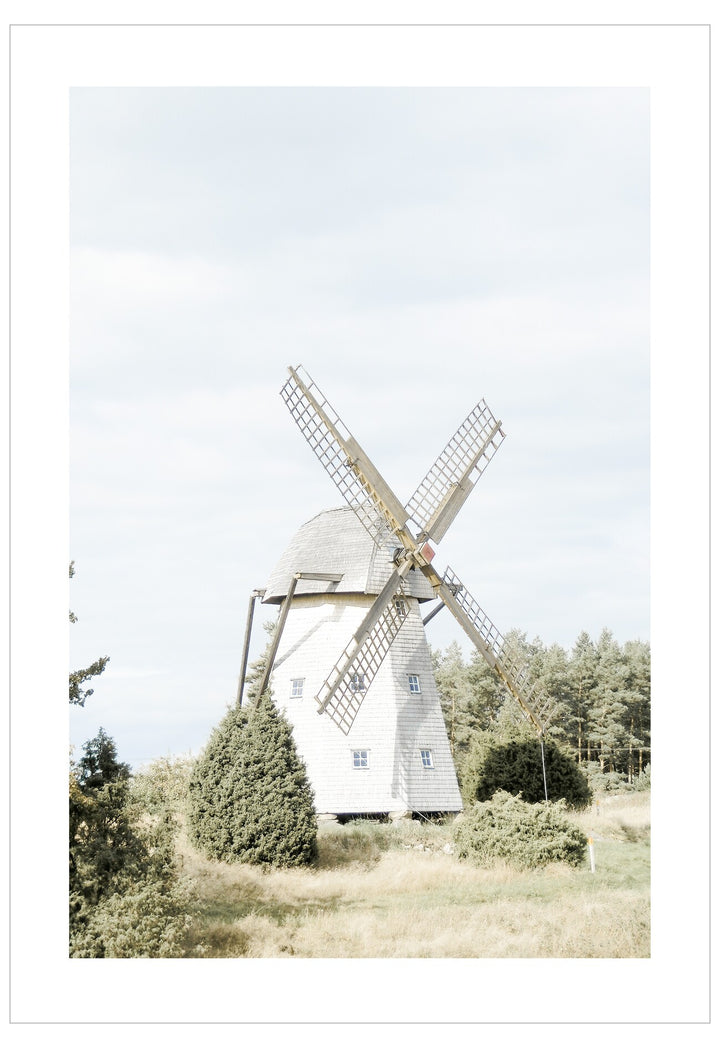 Traditional windmill in a rural landscape with trees and clear sky.