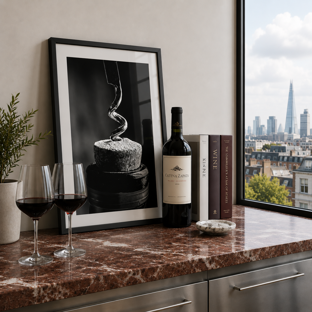 Wine bottle, glasses, and books on a marble countertop with a cityscape view.