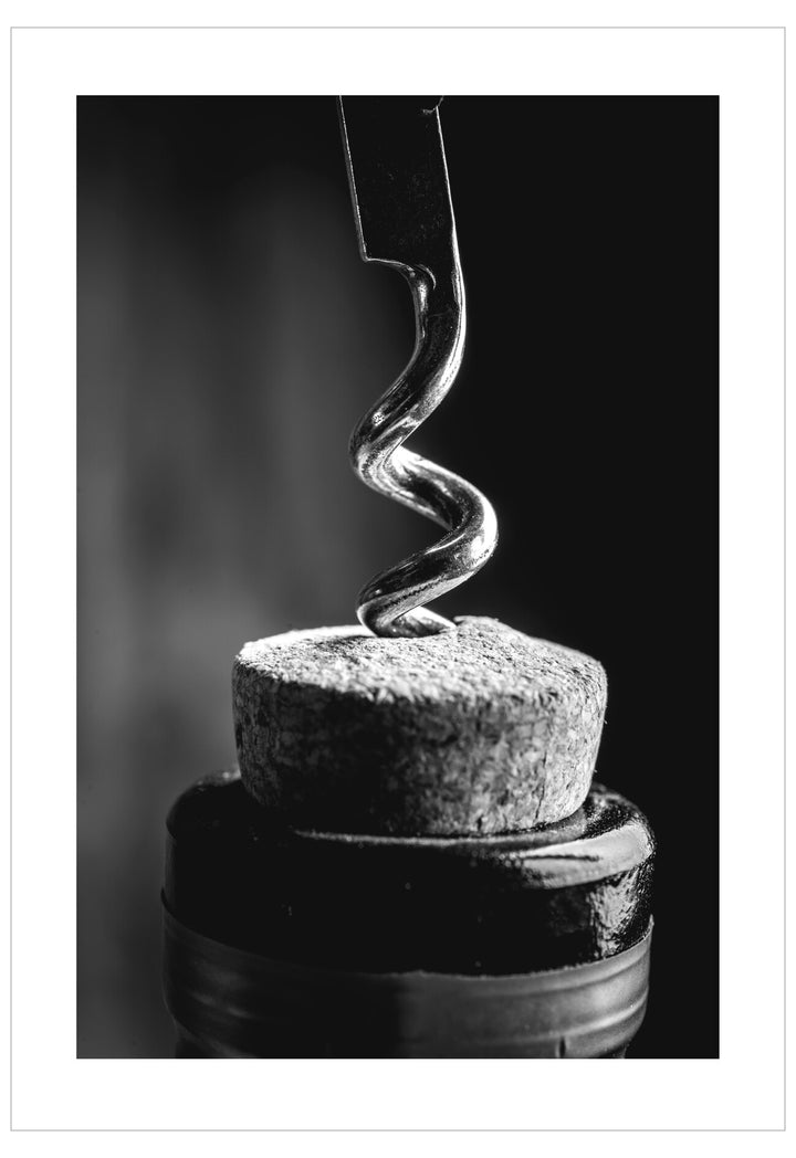 Corkscrew inserted into a cork on a dark background