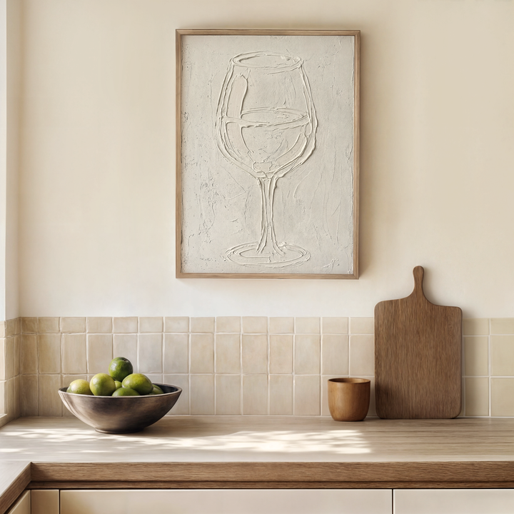 Modern kitchen with a wooden cutting board, bowl of apples, and abstract wine glass painting on the wall.
