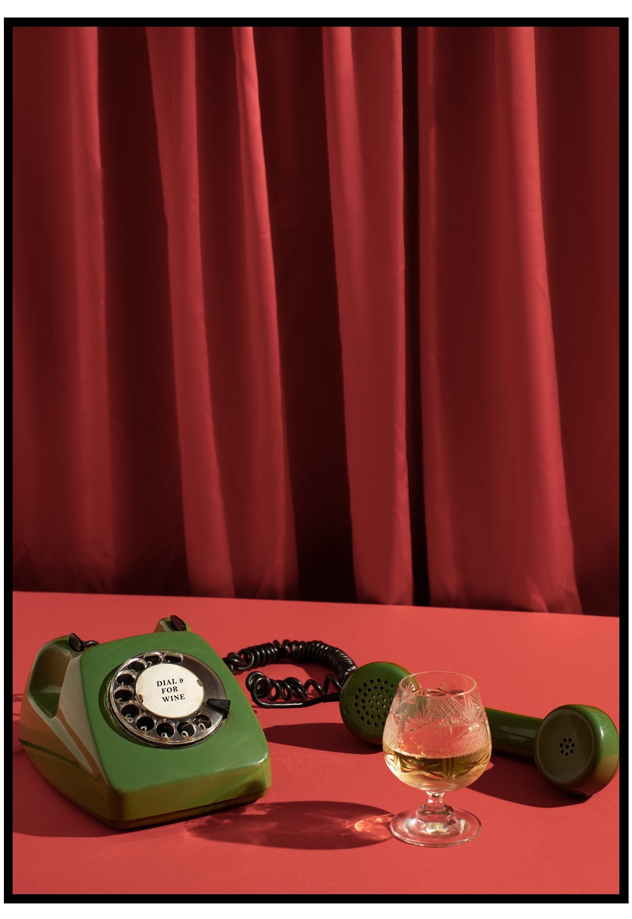 Green rotary phone, glass of whiskey, and dumbbells on a red surface with red curtains in the background.