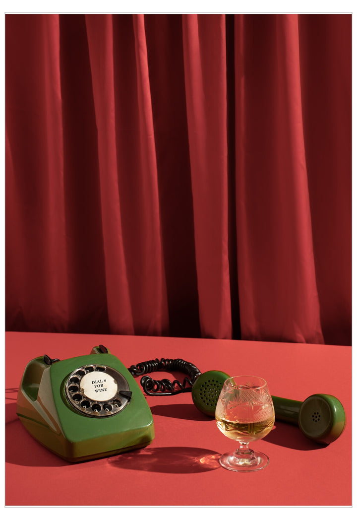 Green rotary phone and glass of whiskey on a red surface with red curtains in the background