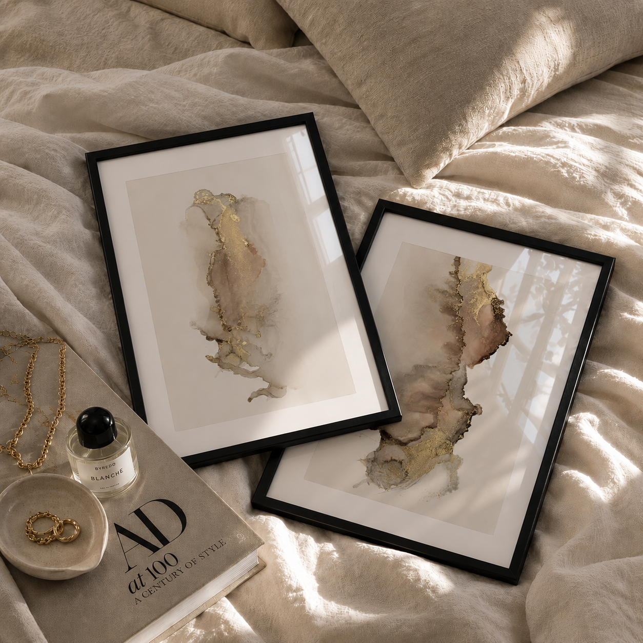 Two framed abstract artworks on a bed with jewelry and a book.