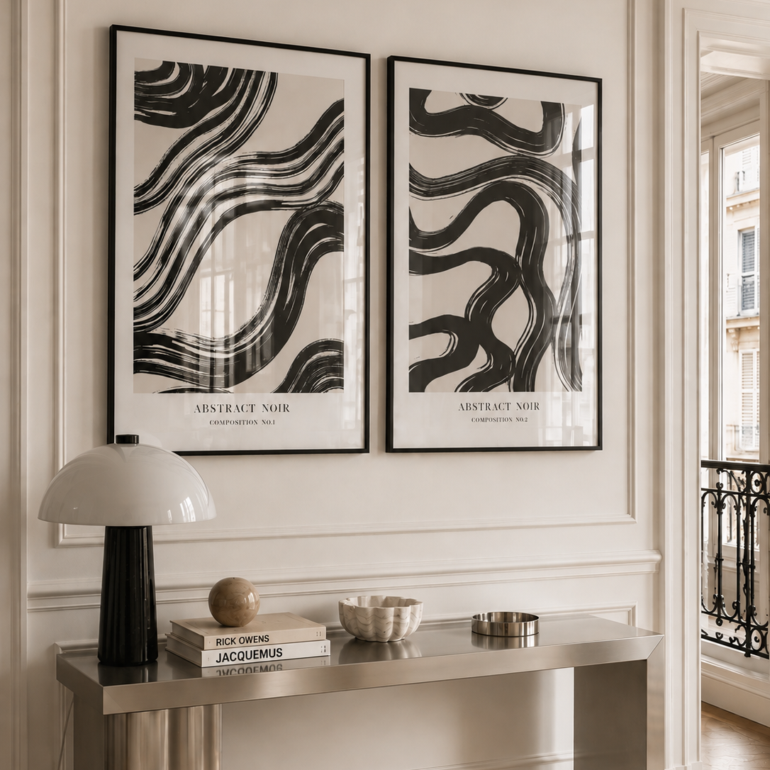 Two framed abstract black-and-white art prints hang on a cream wall above a metallic console table in a styled interior room.