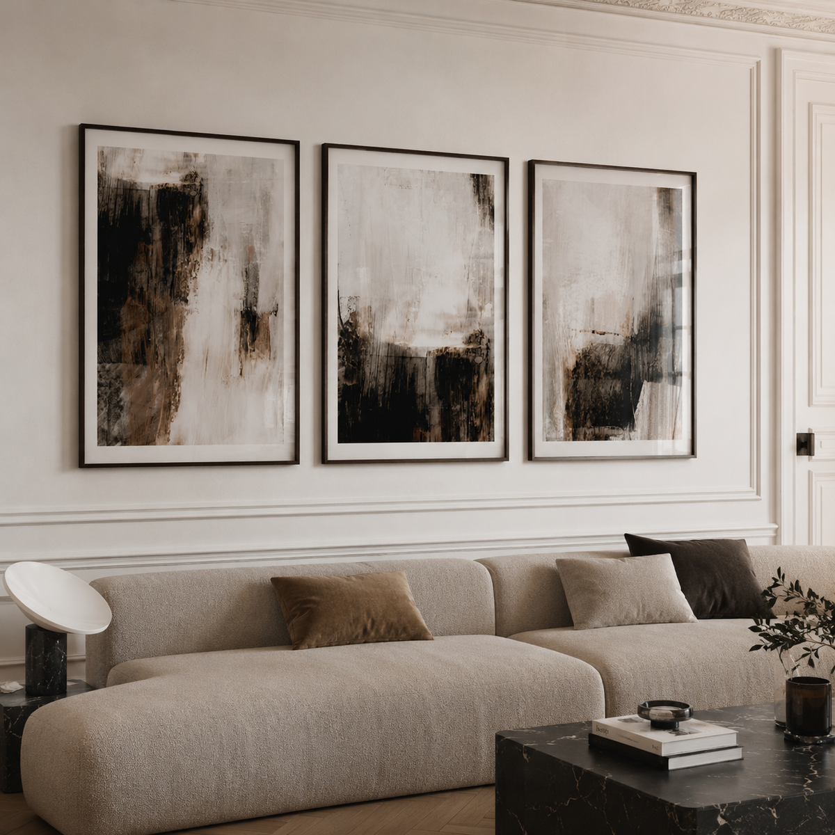 Three framed abstract wall art prints in black, white, and brown tones are displayed above a beige sectional sofa in a styled living room.
