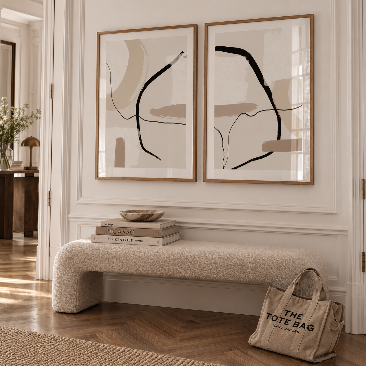 A styled interior scene showing two framed abstract wall art prints hanging above a cream boucle bench. The prints have minimalist black and beige line drawings in light wood frames.