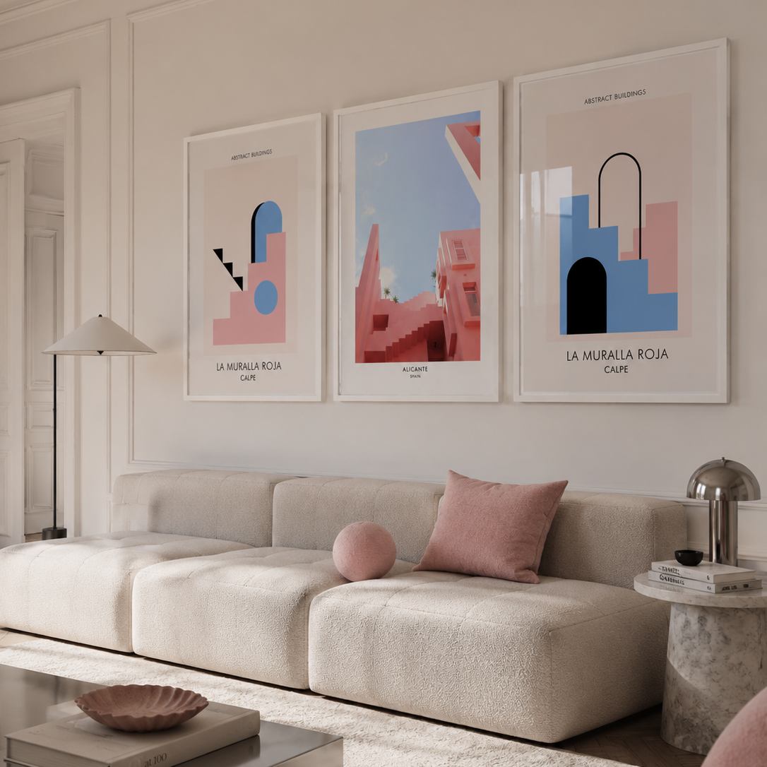 Three framed abstract art prints in pink, blue, and coral tones hang on a cream wall above a beige sofa in a modern living room.