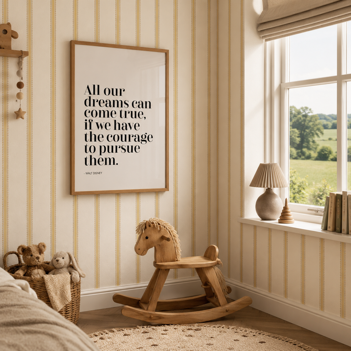 A framed wall art print with a motivational quote hangs on a cream and tan striped wallpapered wall in a styled children's room corner, featuring a rocking horse, teddy bears, a window, and a lamp.