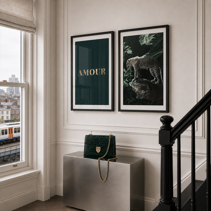 Two framed wall art prints hang above a metallic side table in a styled interior. The left print is dark green with the word 'AMOUR' in gold, and the right print shows a leopard in a jungle scene.