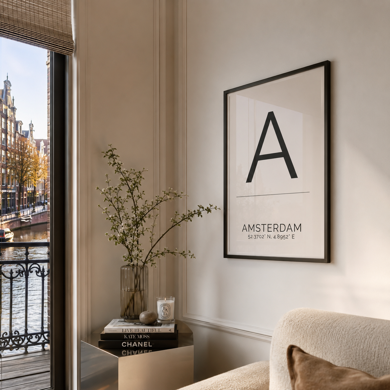 A framed minimalist poster featuring the letter 'A' and the text 'AMSTERDAM' hanging on a cream wall in a modern living space next to a window overlooking a canal.